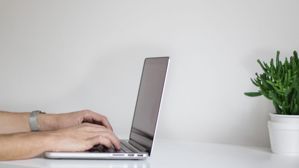 Side view of a laptop being used by a pair of hands on a white background