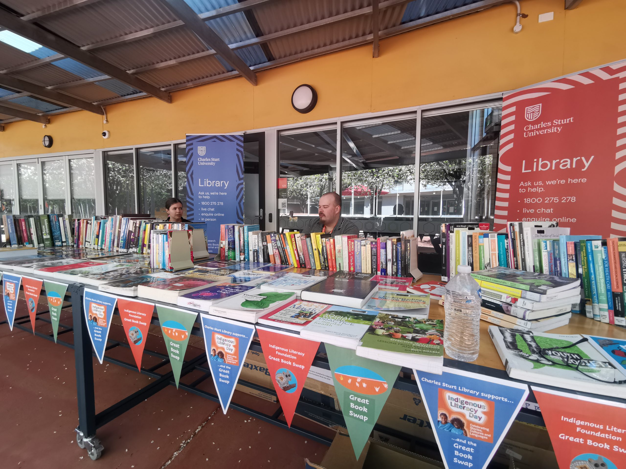 Library staff at the Great Book Swap stall in Dubbo. They are seated behind a large table filled with books.