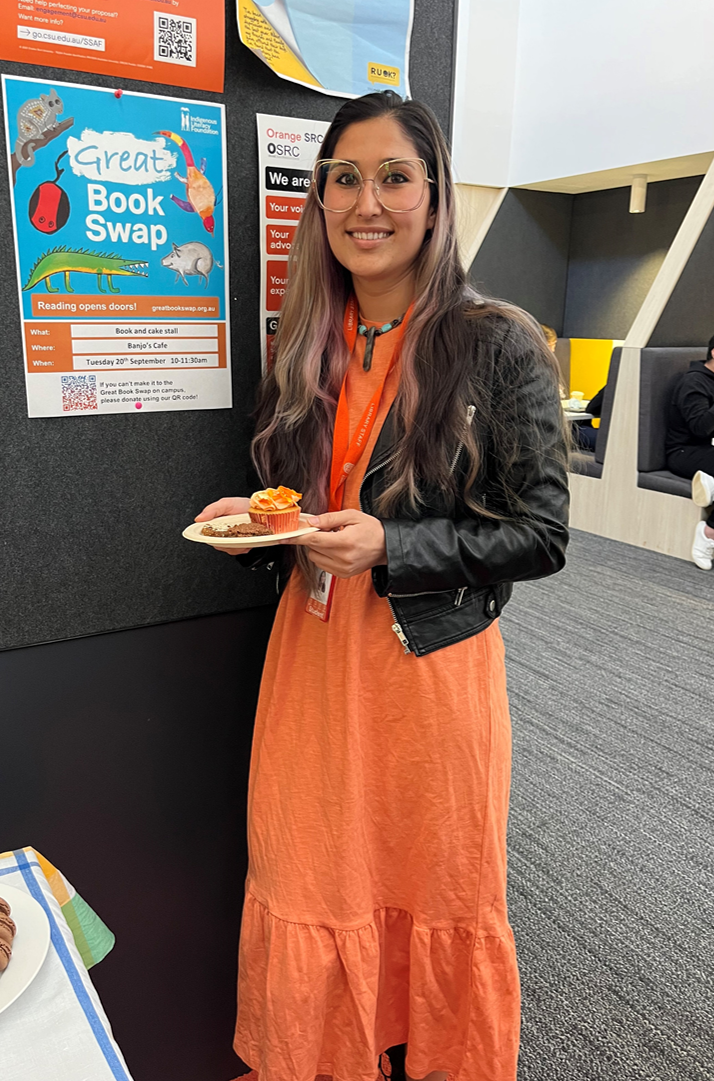 Student Rohina at the Great Book Swap In Orange. Rohina is wearing an orange dress and holding an orange cupcake.