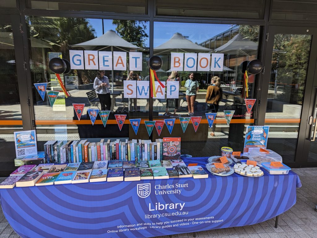 Outdoor table covered with books and plates of cakes.