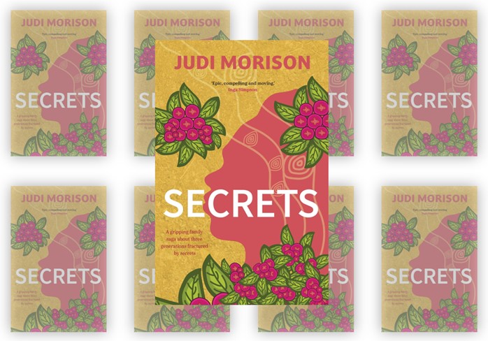 A stylised book cover featuring the silhouette of a head filled with swirling decorative patterns against a textured gold background. Bright pink and green botanical illustrations frame the design. The title Secrets appears in large white letters, with the author’s name, Judi Morison, displayed at the top.